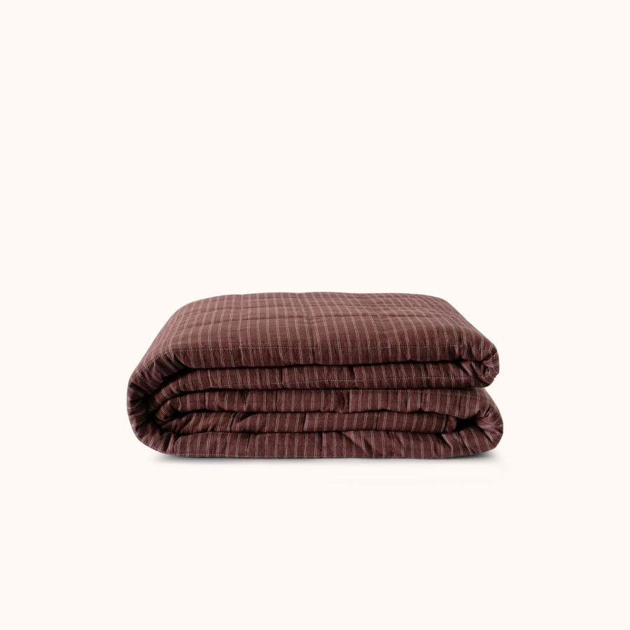 Folded brown striped quilt / bedcover / coverlet against a white background