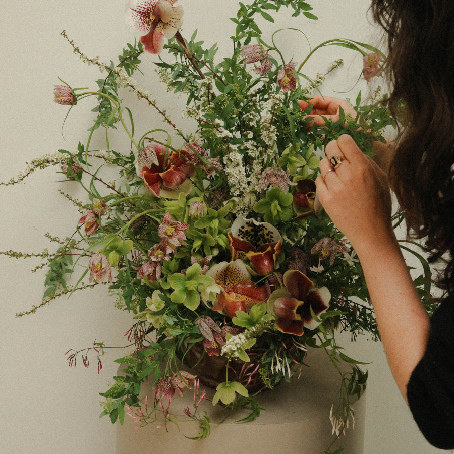 A close-up of a person arranging a large, lush wildflower arrangement.