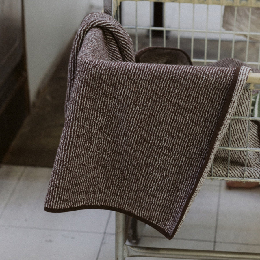 A dark brown and beige textured woven towel draped over a metal cart in an indoor setting.