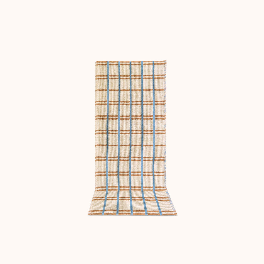 A rectangular, runner with a geometric checkered pattern in blue and tan on a natural beige background, designed for use as a kitchen or bath mat.