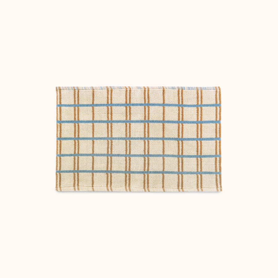 A checkered bath mat with blue and tan stripes on a natural beige background.