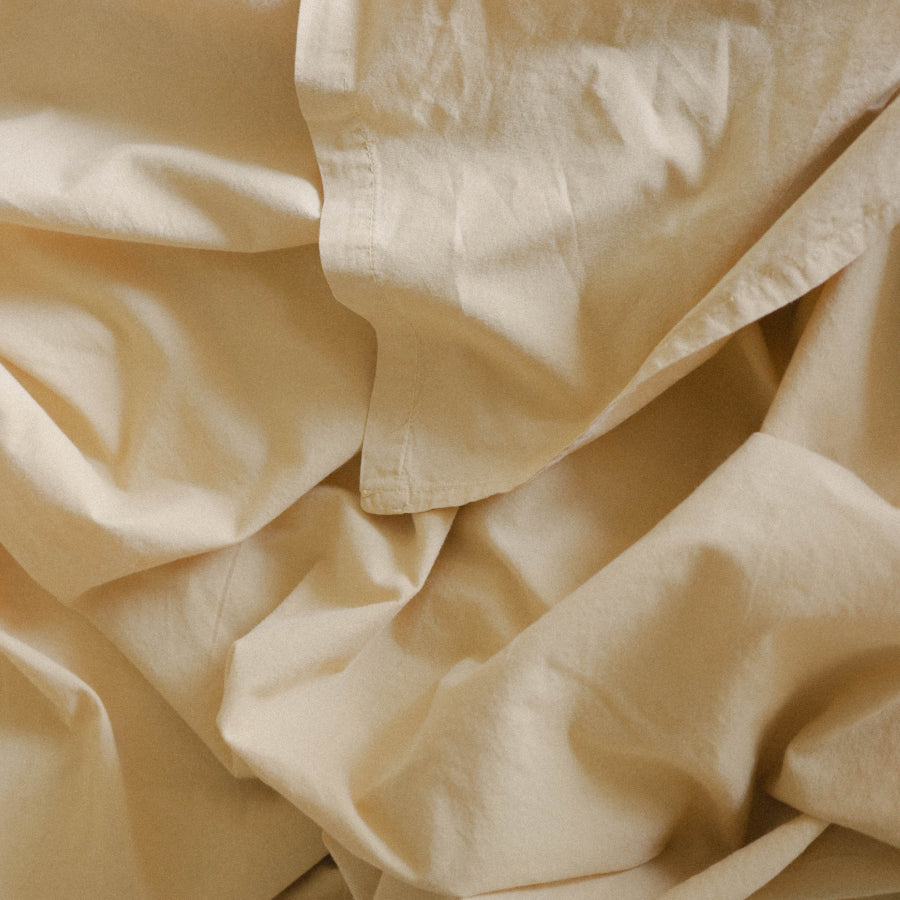 A close-up of draped pale yellow fabric with soft folds and a matte texture.
