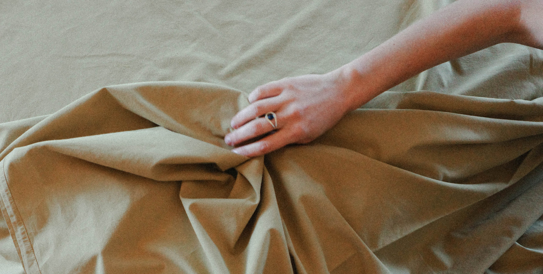 A close-up of a person's hand resting on draped pale olive fabric, with a ring visible on one finger.