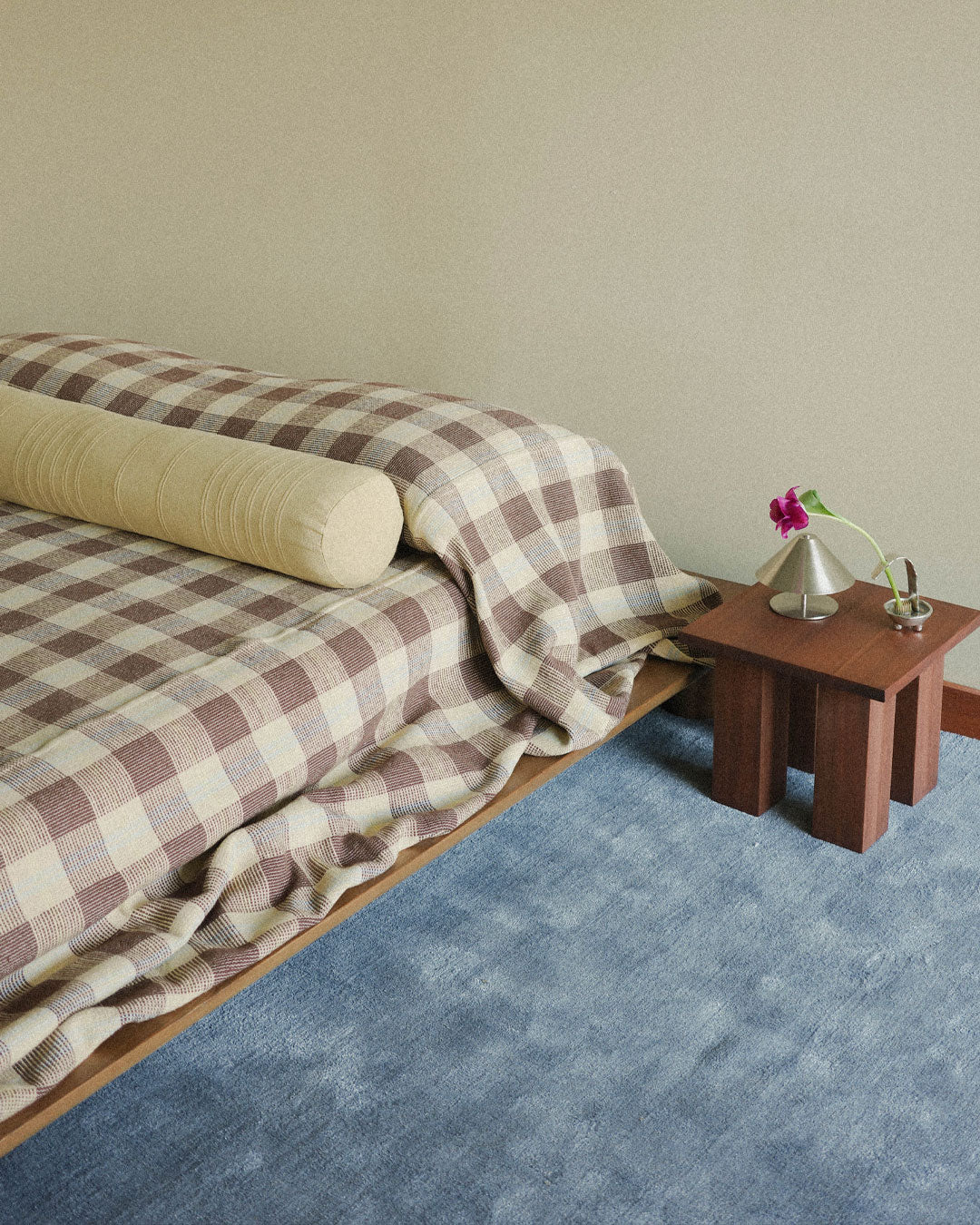 Bed with checkered blanket and wooden side table in a minimalistic room.