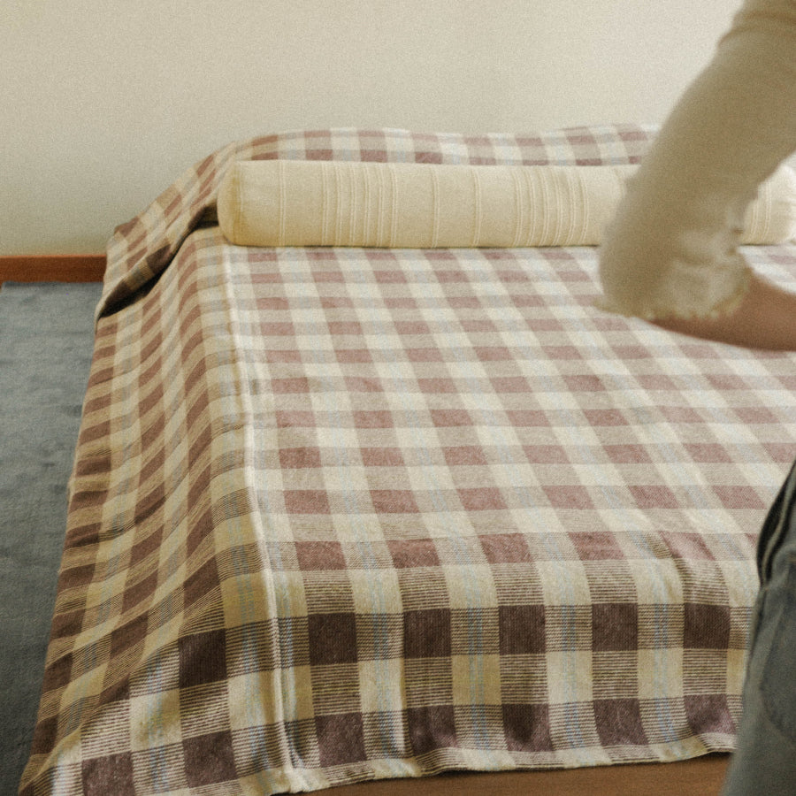 A person standing in front a bed dressed in a brown check blanket and long yellow bolster pillow.