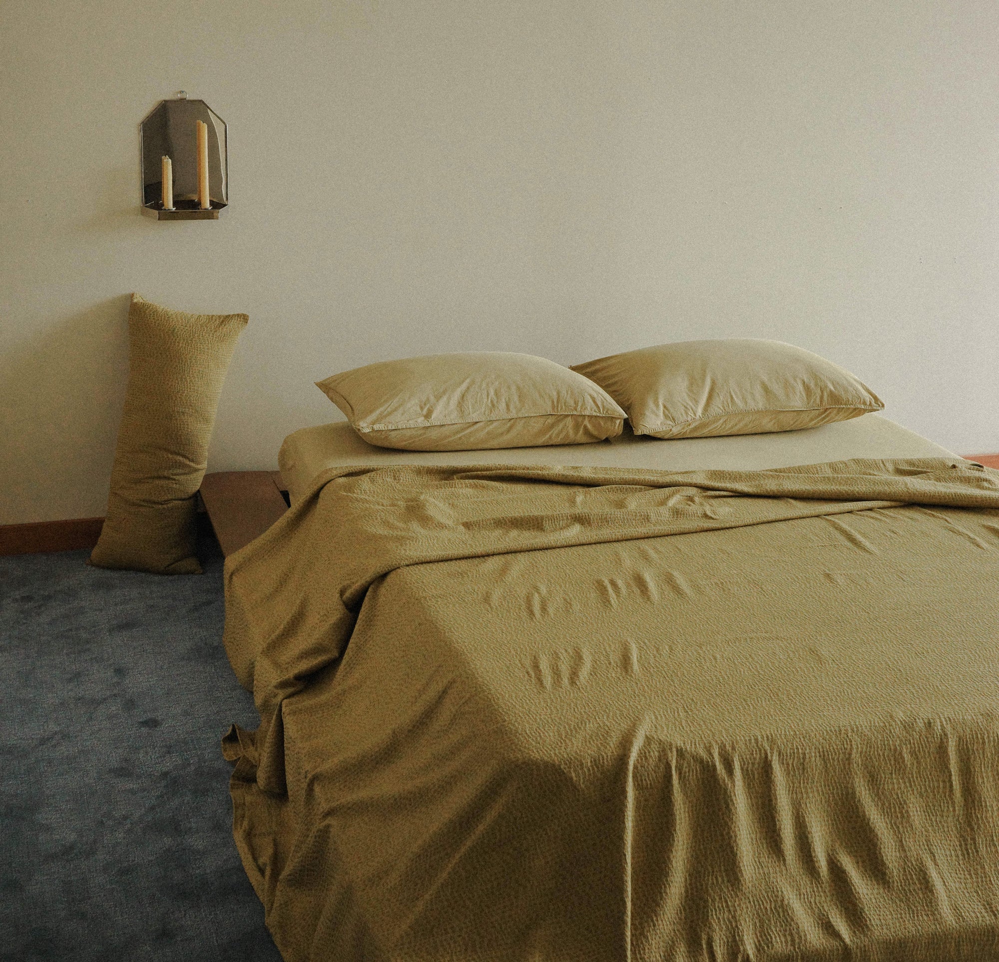 Bed with light green bedding and pillows in a minimalistic room.