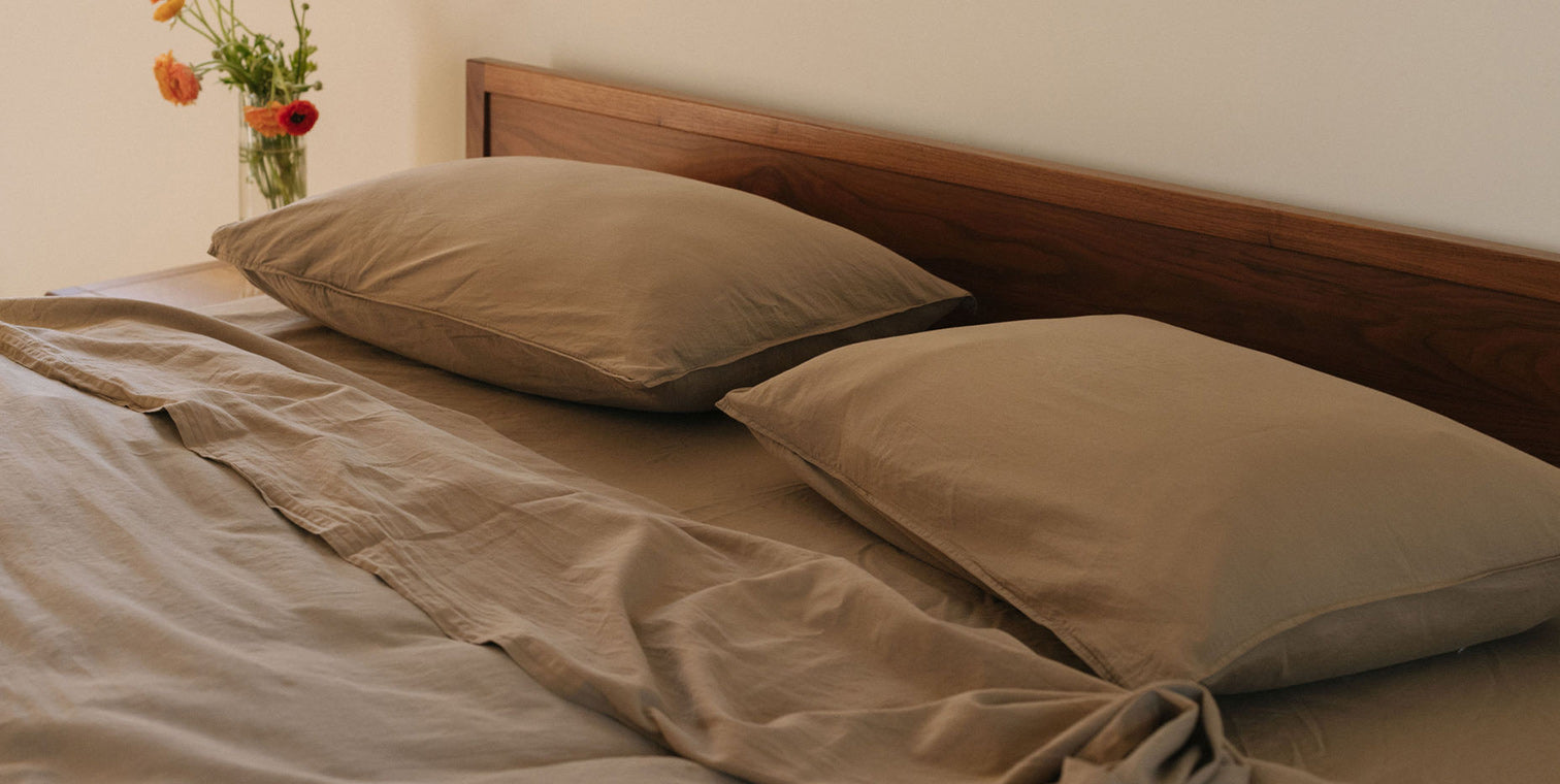Light brown bedding on a bed with a wooden headboard and flowers in the background.