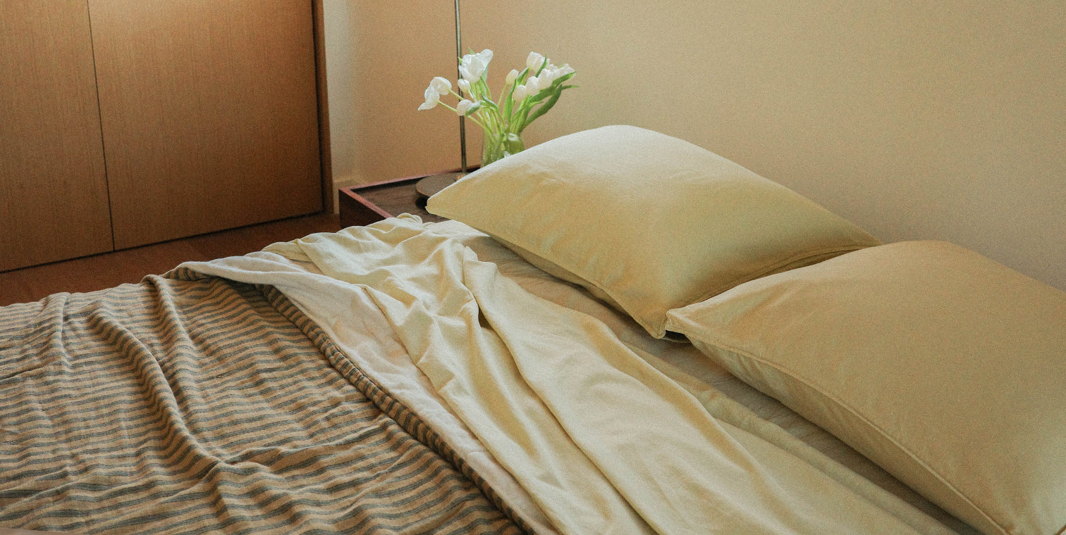 Bed with yellow pillows and a striped blanket, next to a wooden cabinet.
