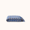 A folded blue patterned woven throw blanket with fringed edges, displayed on a clean off-white background.