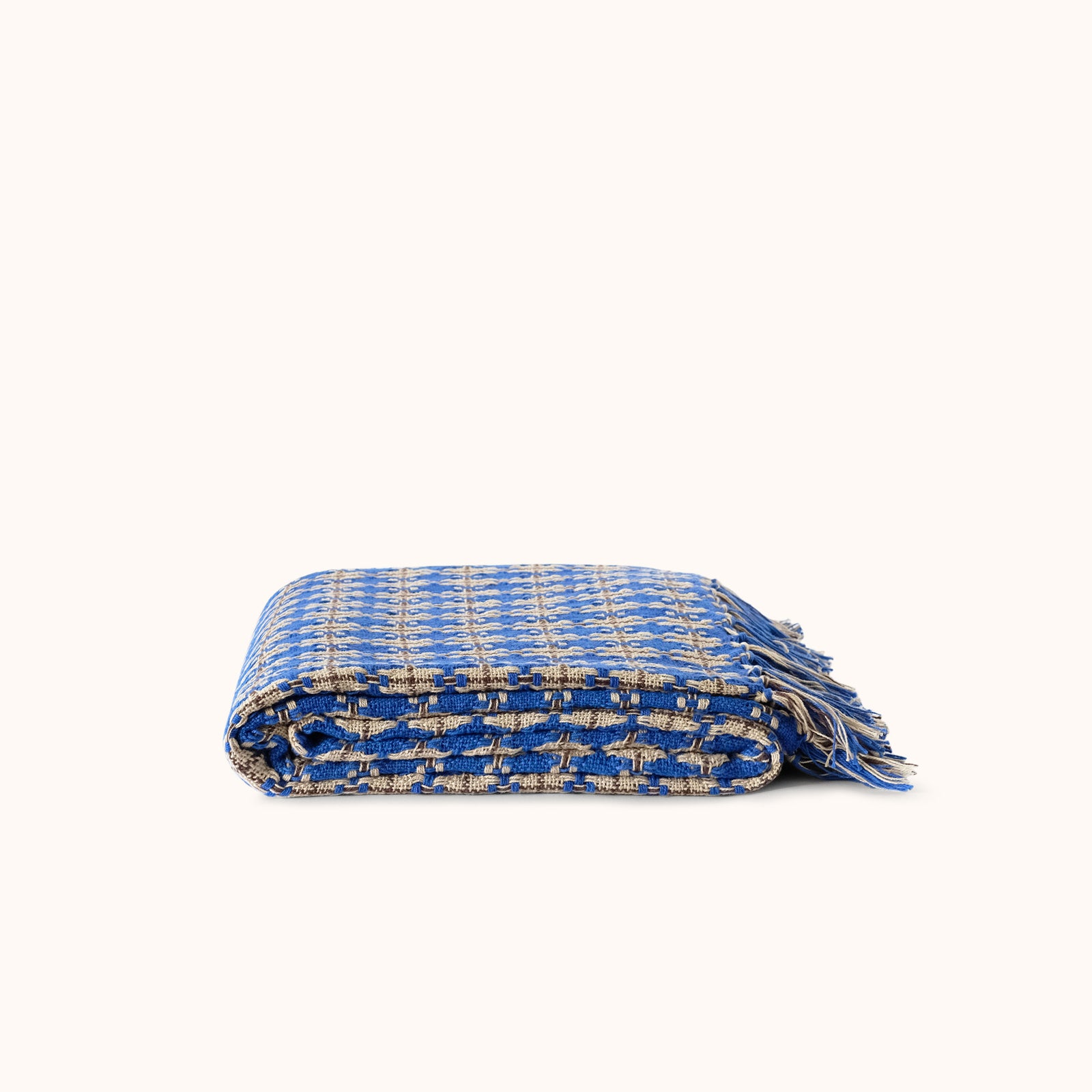 A folded blue patterned woven throw blanket with fringed edges, displayed on a clean off-white background.