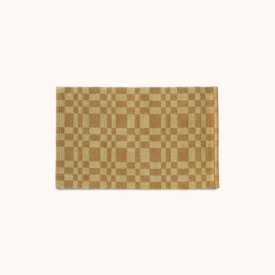 A rectangular mat with a pale olive and light brown checkerboard pattern, displayed flat against a solid off-white background.