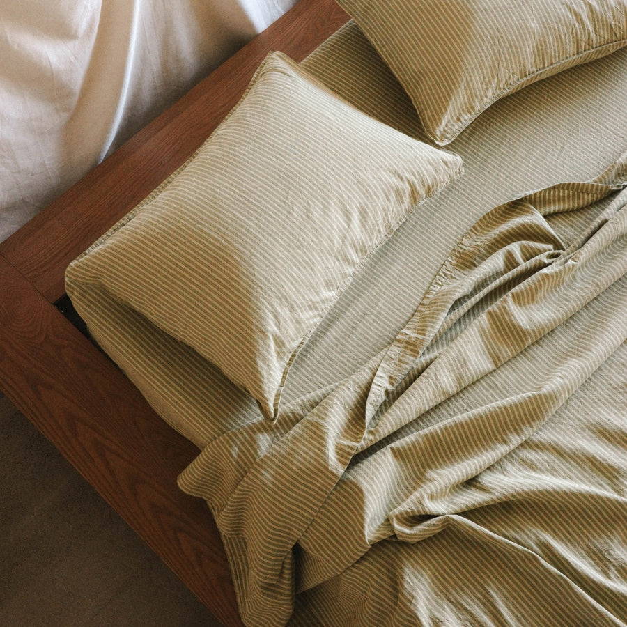 A close-up of a bed dressed in green striped bedding, styled on a dark wood bed frame.