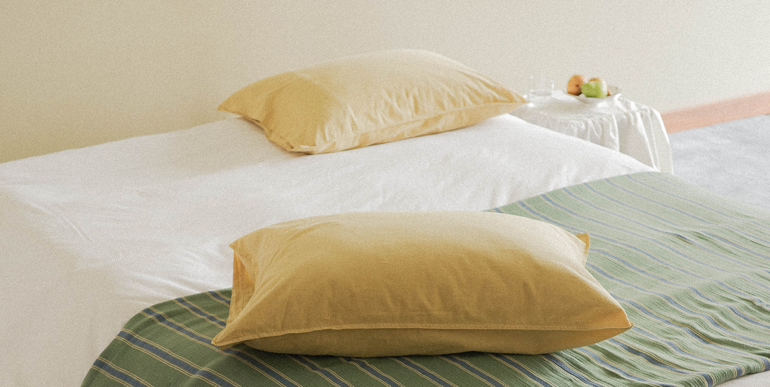 Two yellow pillows on a bed with a green and white striped blanket.