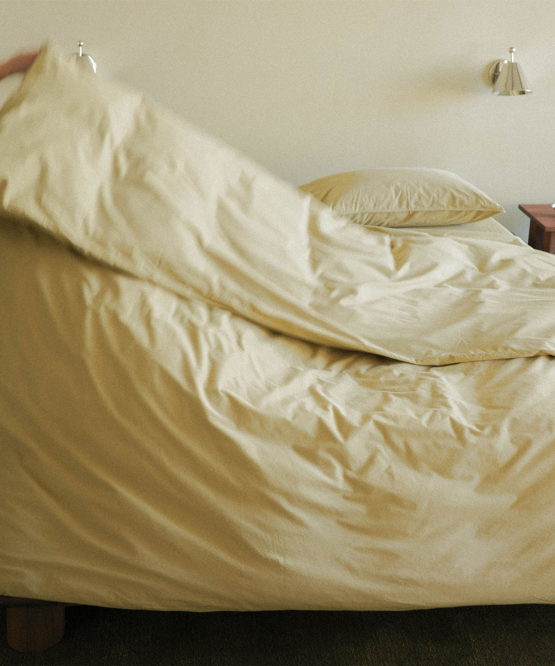 Person fluffing a green duvet on a bed