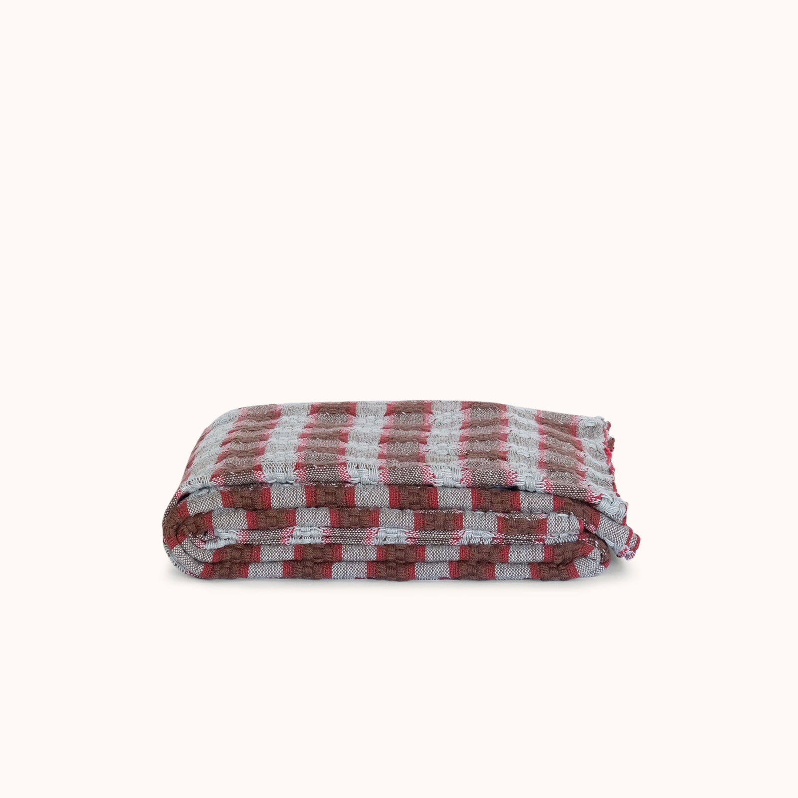 A folded checkered blanket with a pattern of red, brown, and blue stripes, displayed on a clean off-white background.