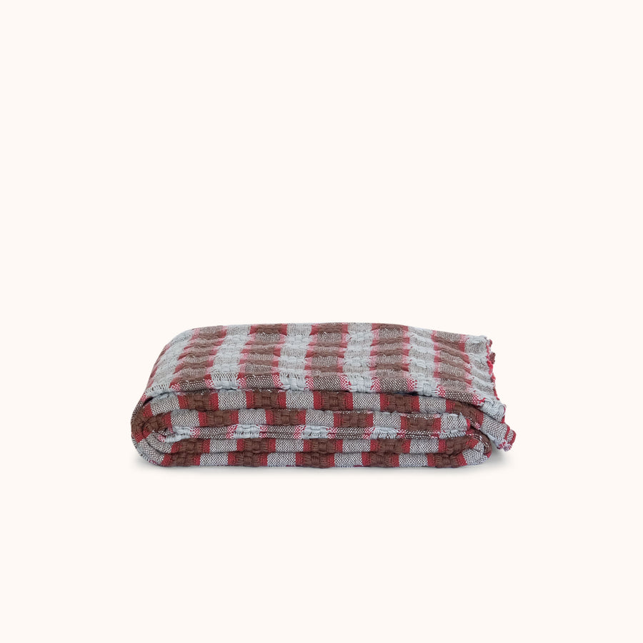 A folded checkered blanket with a pattern of red, brown, and blue stripes, displayed on a clean off-white background.