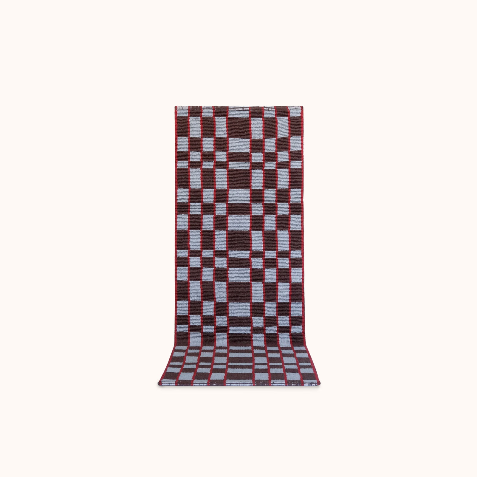 A long rectangular woven mat featuring a geometric checkerboard pattern in light blue, red and plum set against a solid off-white background. 