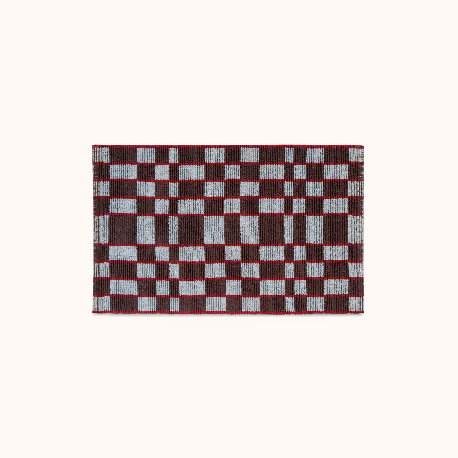 A rectangular woven mat featuring a geometric checkerboard pattern in light blue, red and plum set against a solid off-white background. 
