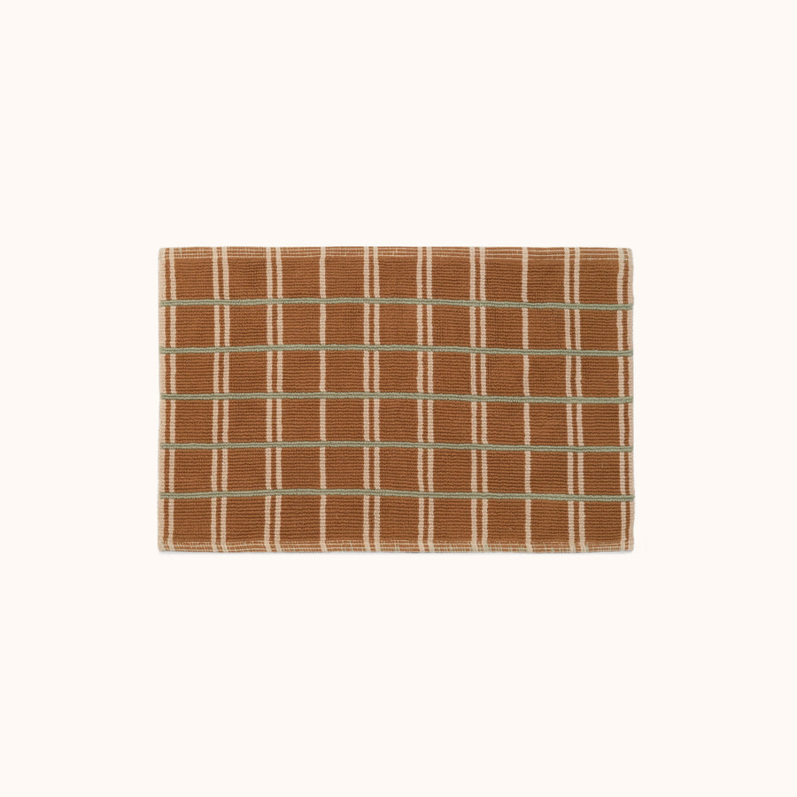 A brown bathmat with horizontal green stripes and vertical tan stripes on a white background.