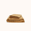 Folded light camel colored sateen sheet set on a white background