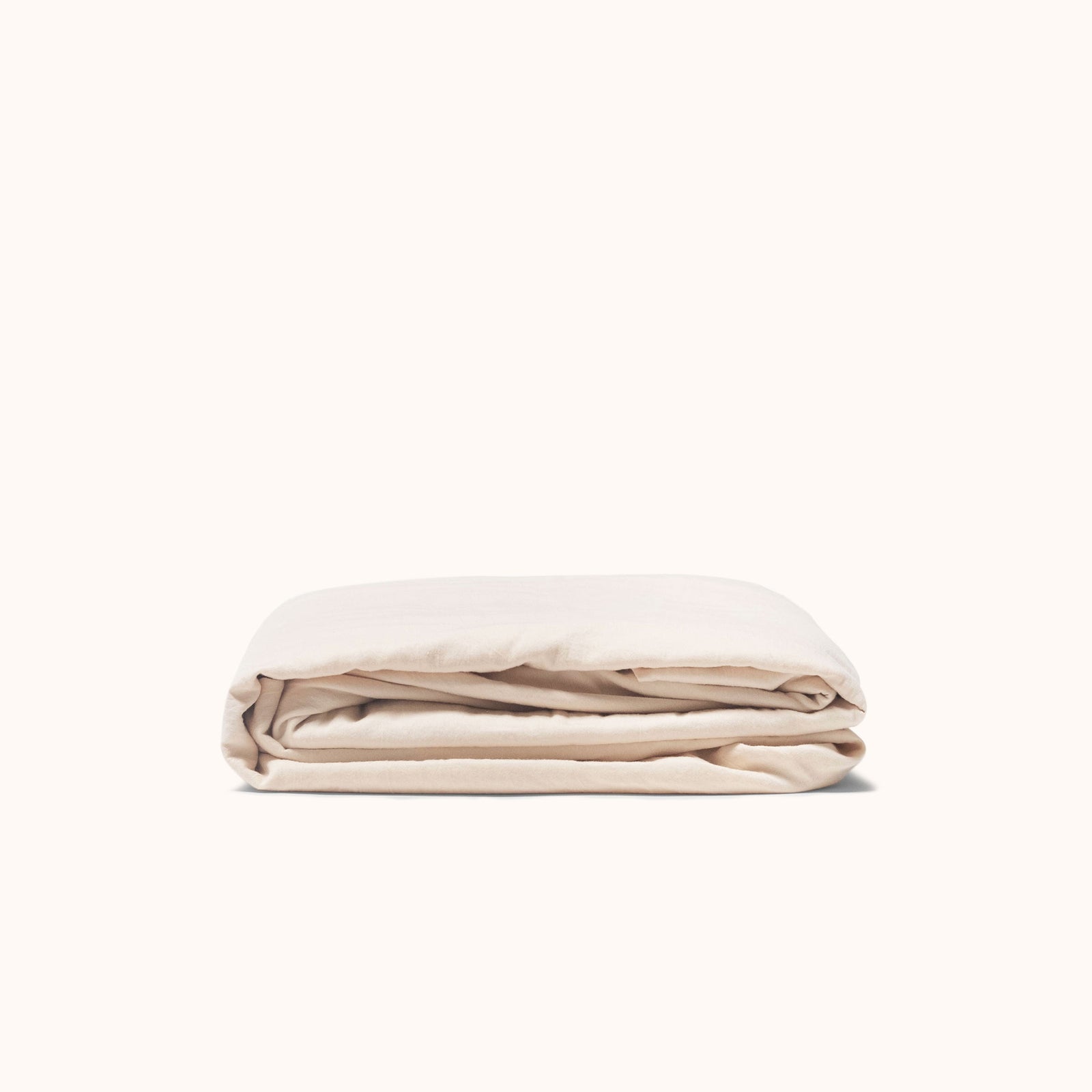 Folded fitted sheet in oat color, made of organic cotton sateen, on a white background