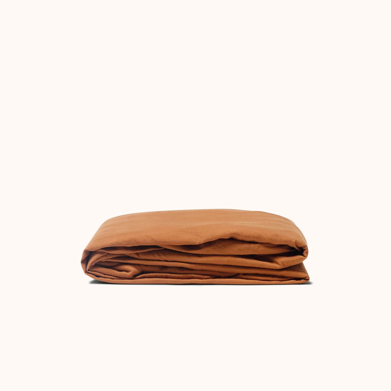 A folded fitted  matte sateen cotton sheet in terracotta against a white background