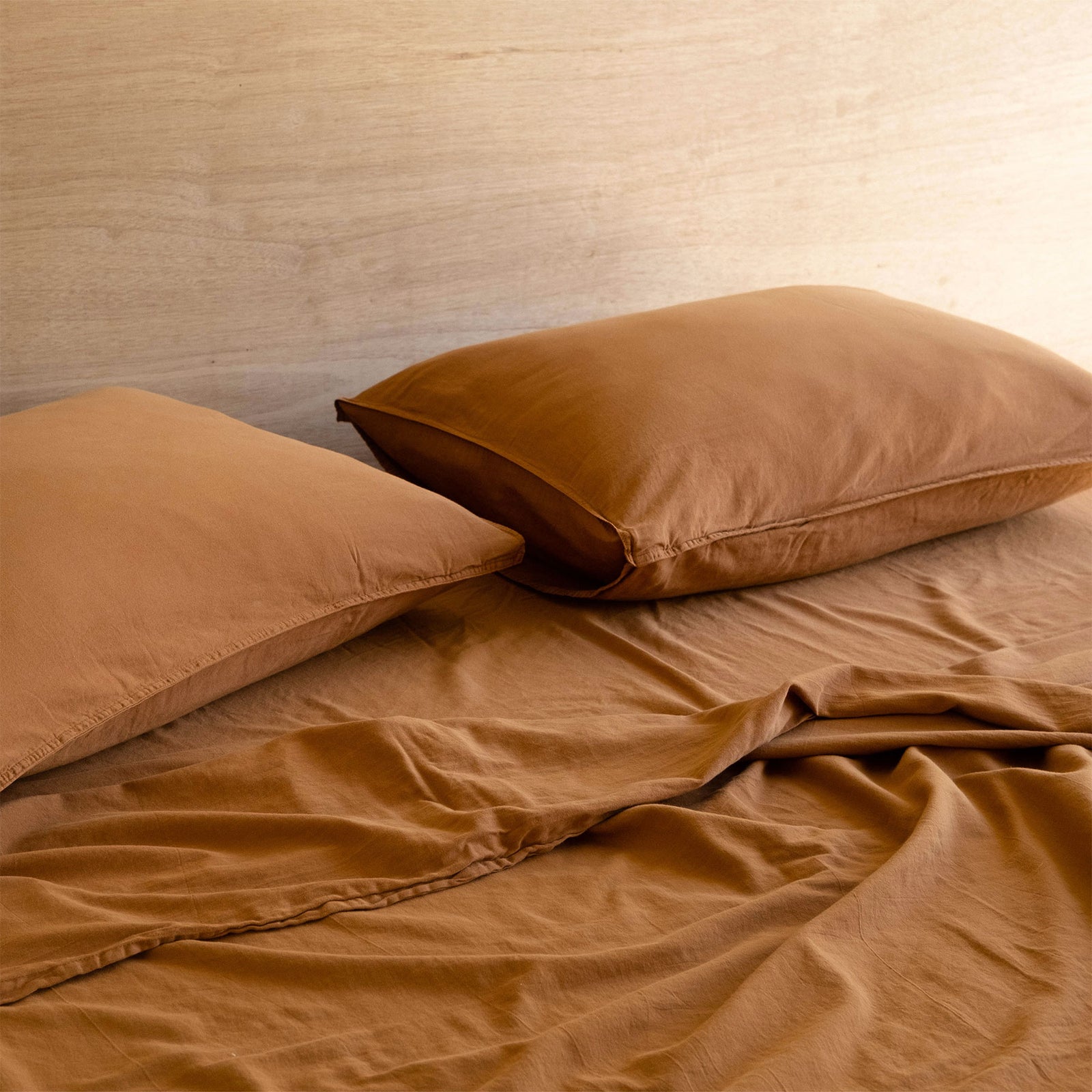 Close up of two pillows and a bed dressed with terracotta / brown cotton matte sateen sheets