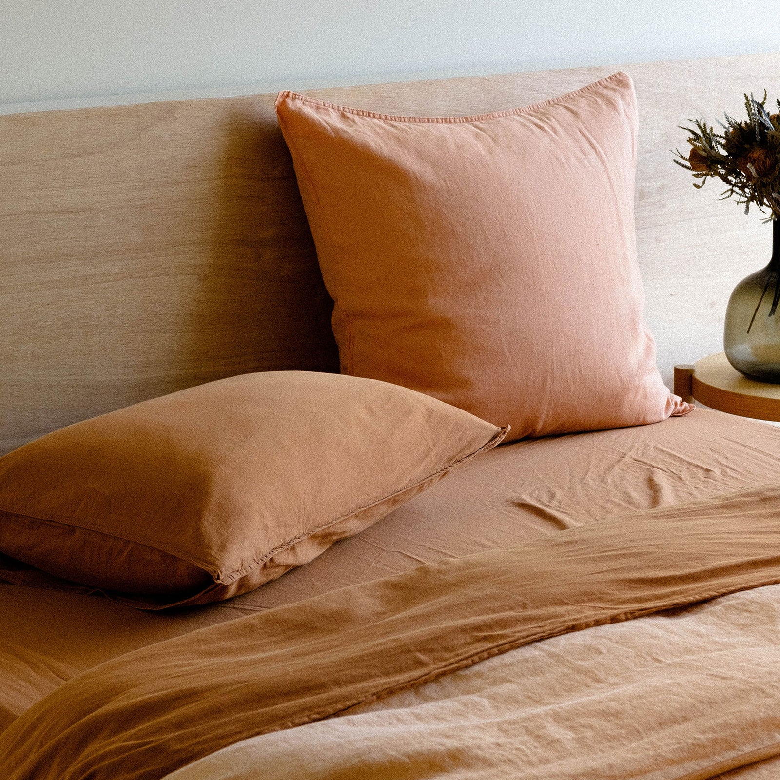 A bed with matte sateen terracotta sheets paired with a peach duvet cover and throw pillow in a bright bedroom