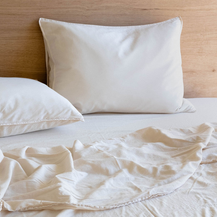 A close up of organic matte sateen oat pillows over slightly rumpled oat sheets. 