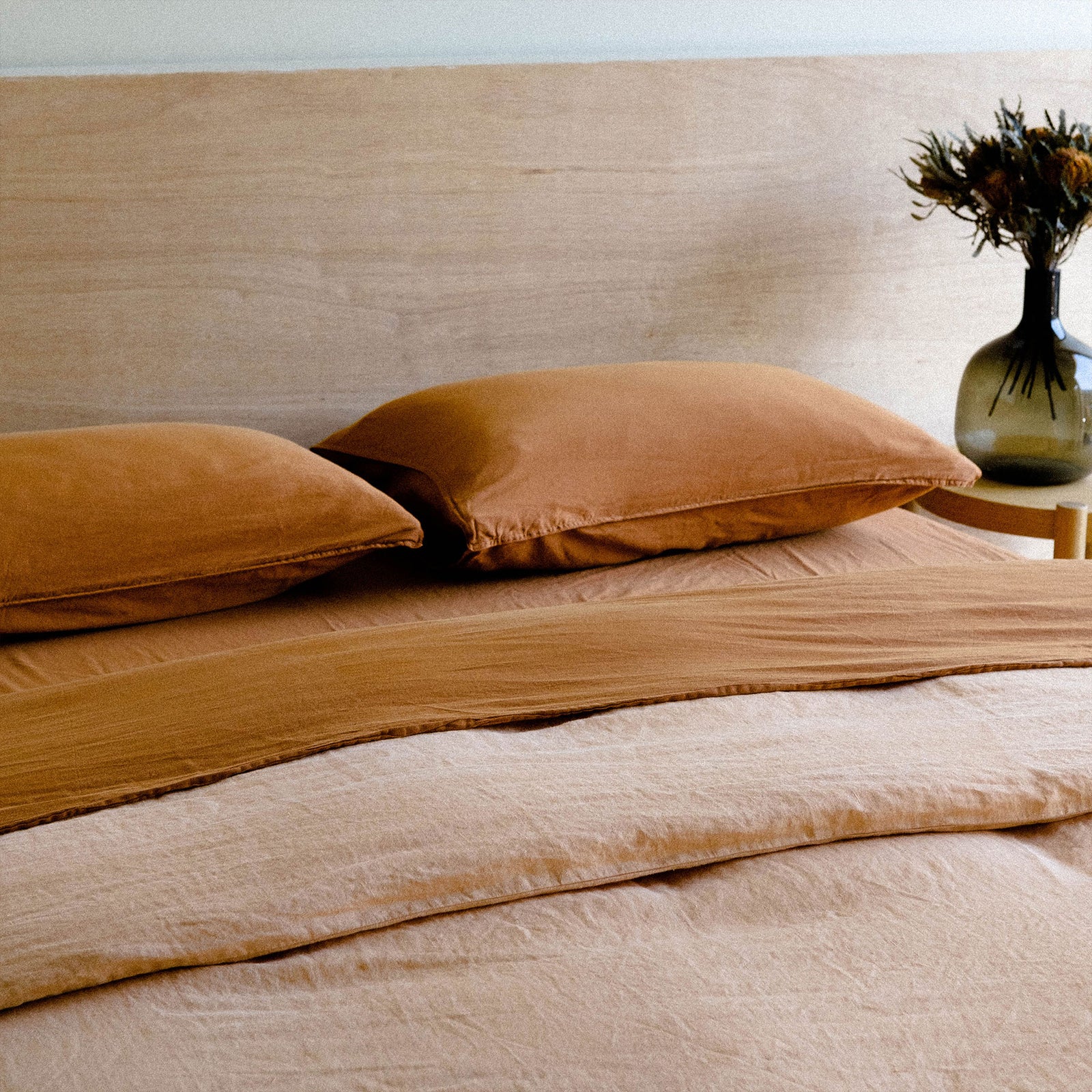A bedroom made with matte sateen terracotta sheets paired with a peach colored duvet cover against a wooden headboard 