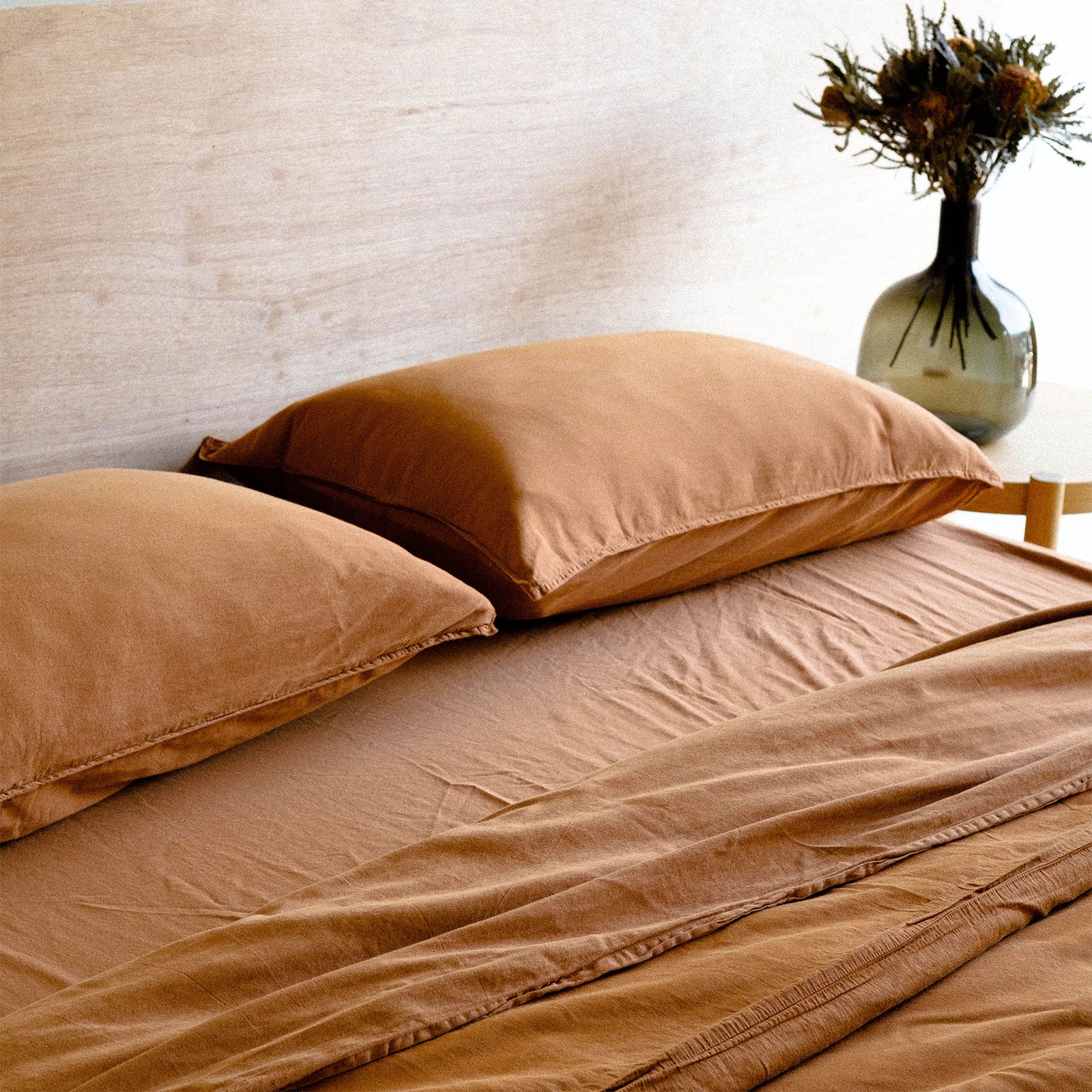 A neatly made bed with matte sateen terracotta sheets and two pillows