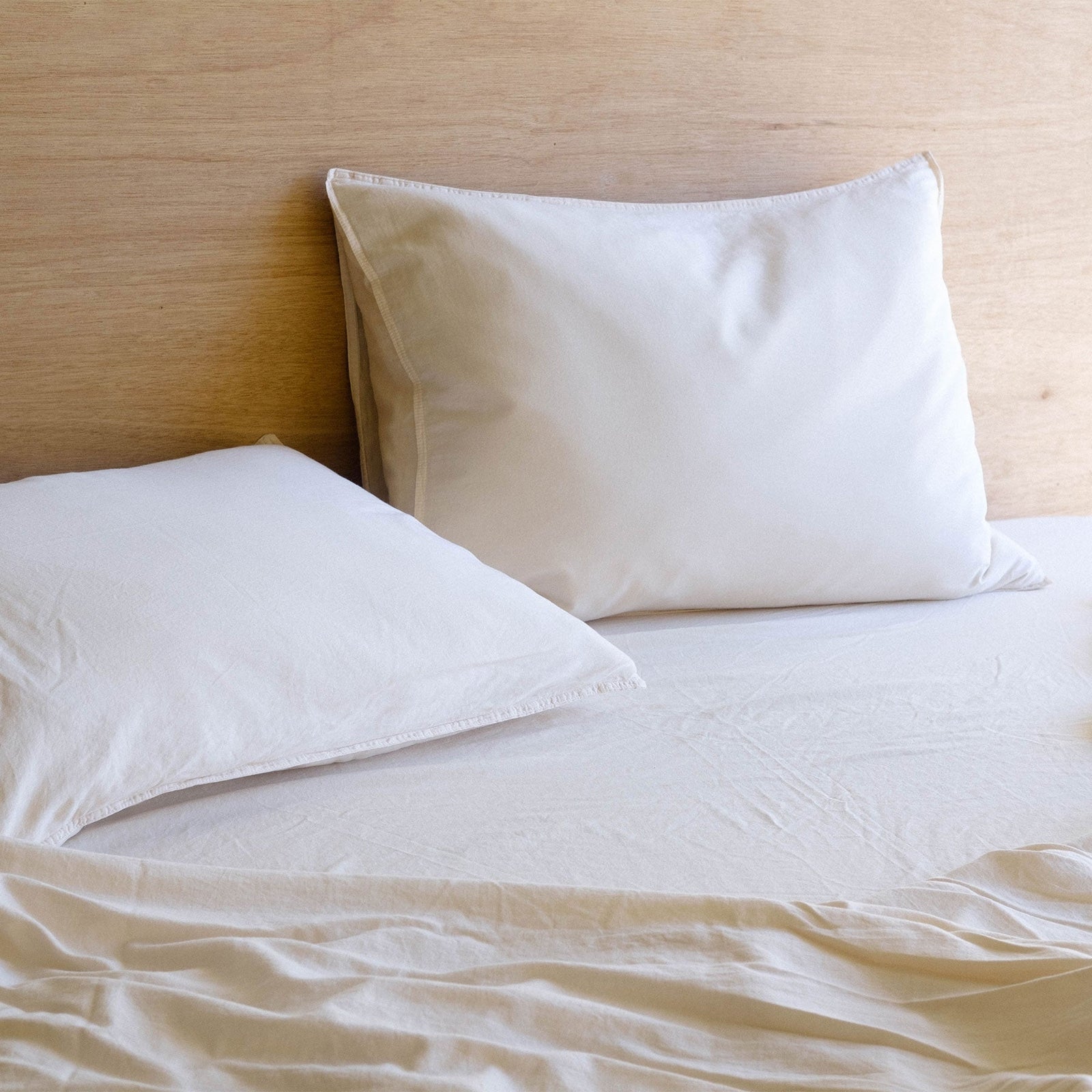 A close up of two organic matte sateen pillows in oat over oat sheets